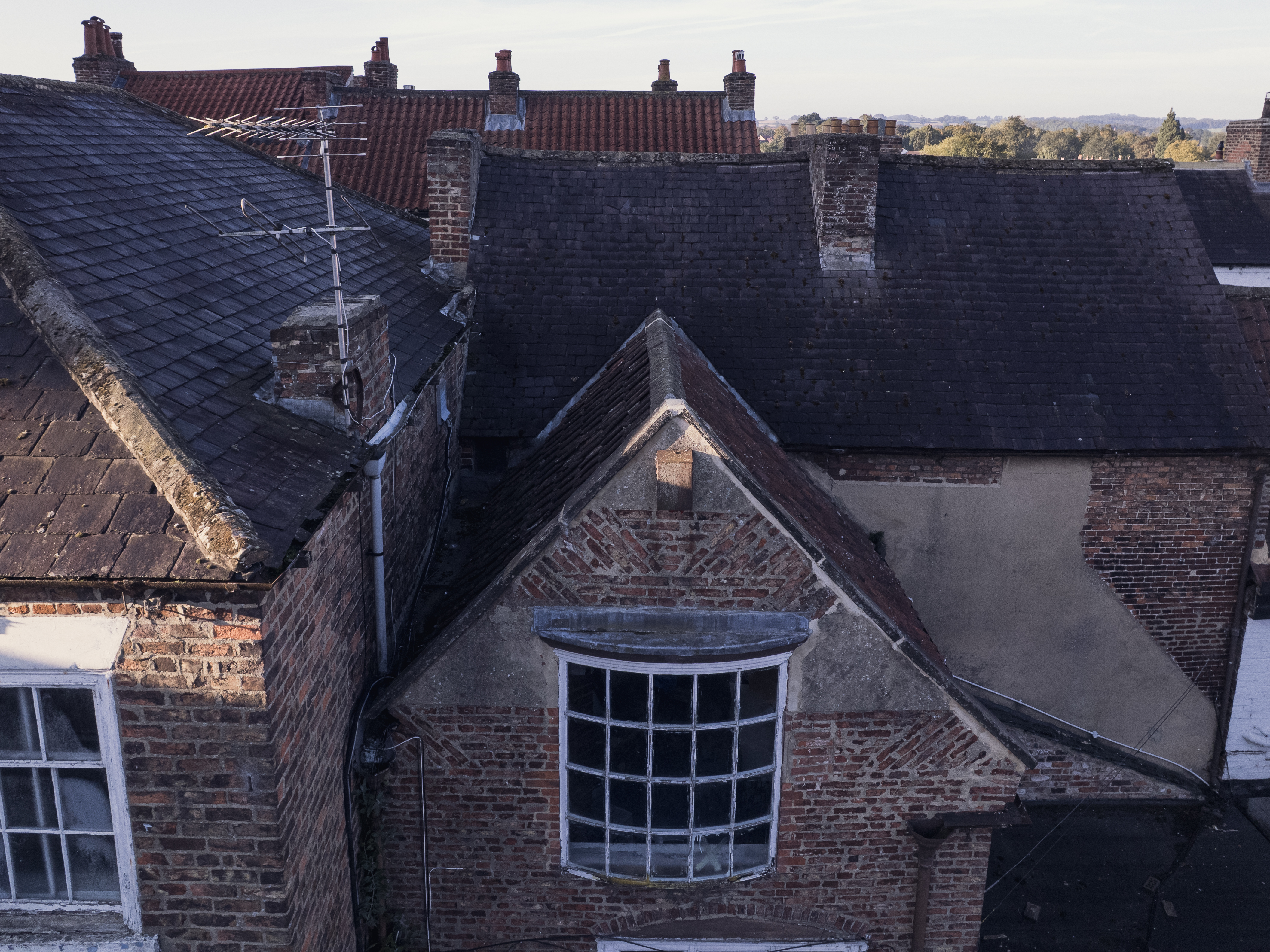 Roofscape of Grade II listed buildings on Kirkgate, Ripon, North Yorkshire — handmade clay pantiles, slate, brick chimney stacks and a bowed sash window, part of a heritage portfolio coordinated by we are _